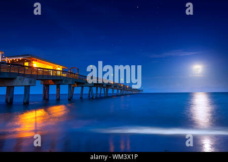 A beautiful full moon rises over the Atlantic Ocean at the Dania Beach Pier in Florida. The Dania Beach Pier is the perfect place to watch the moon. Stock Photo