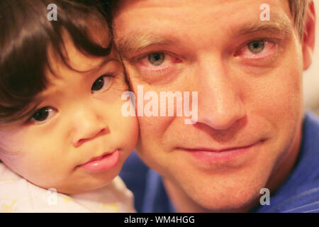 Unhappy baby being comforted by tired father with bloodshot eyes in wee hours of morning. Stock Photo