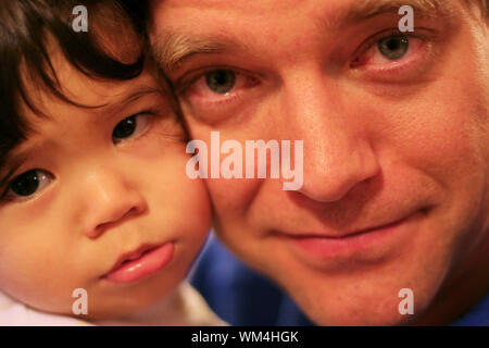 Unhappy baby being comforted by tired father with bloodshot eyes in wee hours of morning. Stock Photo