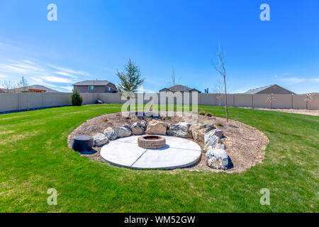 Circular fire pit surrounded by rocks in the middle of the grassy yard of a home Stock Photo