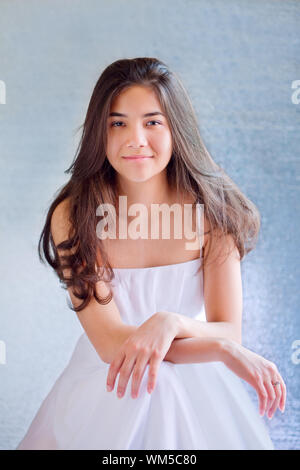 Beautiful biracial teen girl in white dress, sitting arms crosse Stock Photo