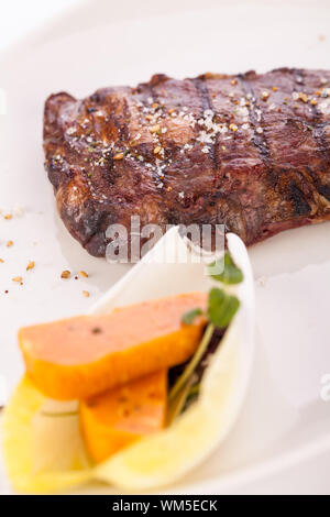 Delicious trimmed lean portion of thick grilled beef steak with seasoning served on a white plate, close up with shallow dof Stock Photo
