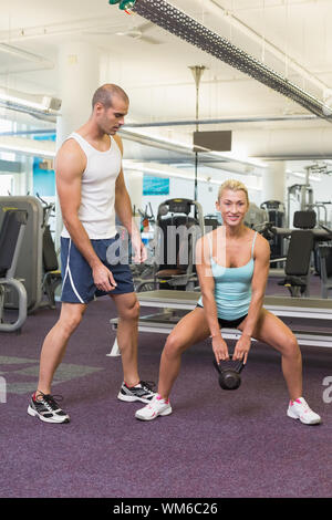 Male trainer assisting woman with kettle bell in the gym Stock Photo