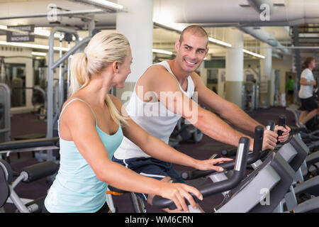 Side view of a fit young couple working on exercise bikes at the gym Stock Photo