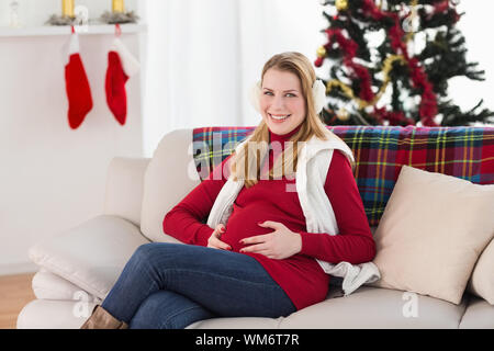 Beautiful pregnant woman holding her belly sitting on couch at home in the living room Stock Photo