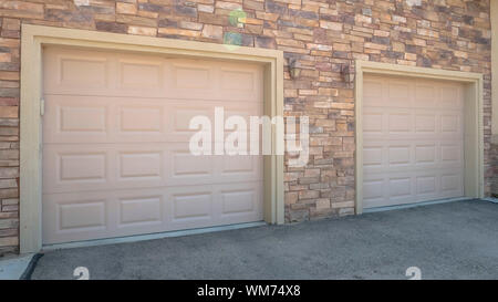 Panorama frame White garage doors of a home against exterior wall covered with stone bricks Stock Photo