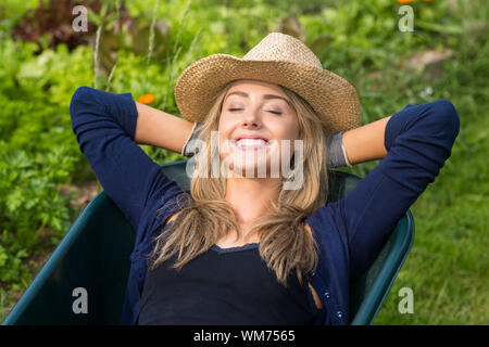 Pretty blonde lying in wheelbarrow at home in the garden Stock Photo