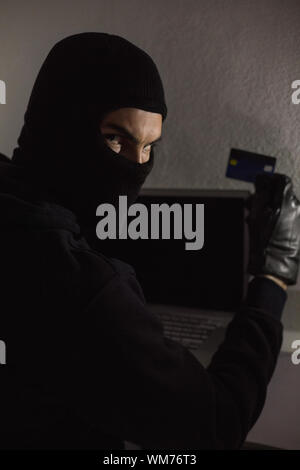 Hacker using debit card and laptop in house Stock Photo