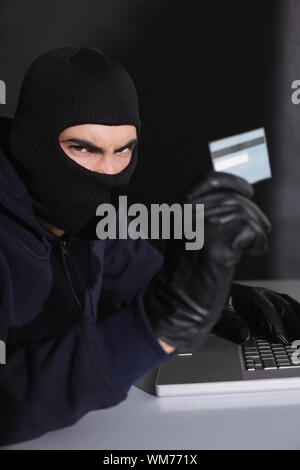 Angry hacker using credit card and laptop on black background Stock Photo