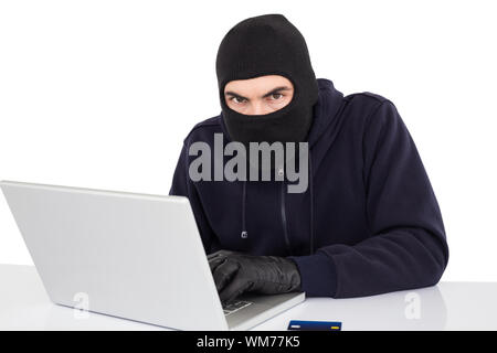 Hacker in balaclava hacking a laptop on white background Stock Photo
