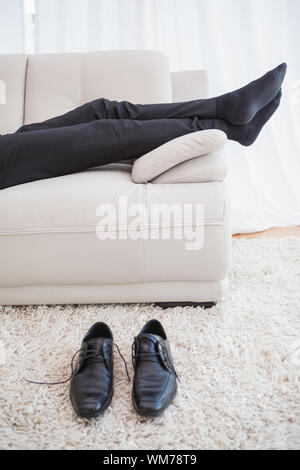 Businessman lying on couch legs only visible at home in the living room Stock Photo