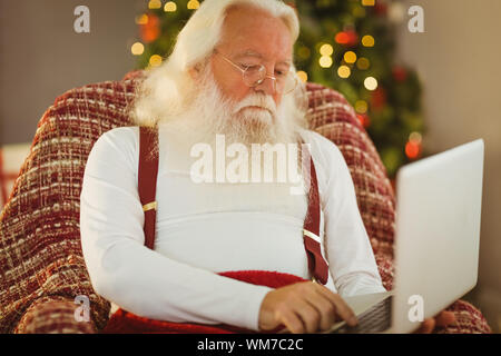 Father christmas typing on laptop at home in the living room Stock Photo