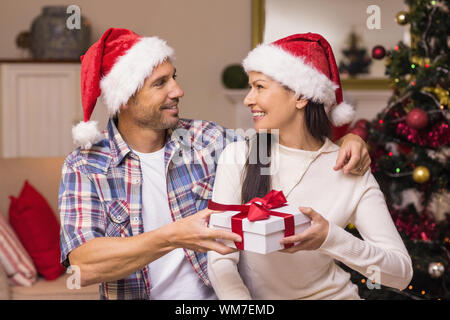 Happy couple in santa hat holding present at home in the living room Stock Photo