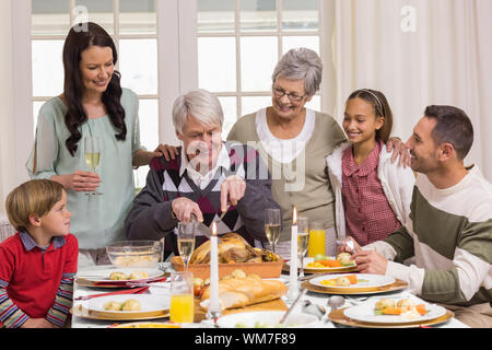 Grandfather carving chicken and his family looking him at home in the living room Stock Photo