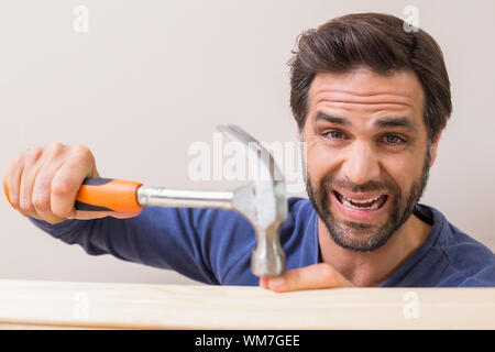 Casual man hammering his finger by accident at home in the living room Stock Photo