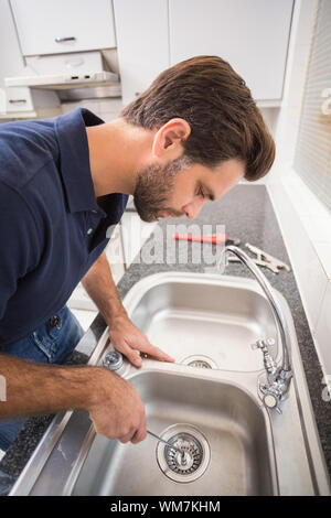 Plumber fixing sink with screwdriver in the kitchen Stock Photo