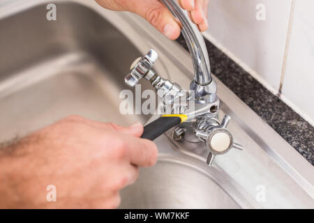 Plumber fixing the sink with wrench in the kitchen Stock Photo