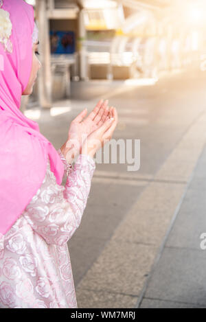 Closed up of young asian muslim woman praying for allah ,Arabian prayer female raising hands pray in hijab prayer. Muslim god outdoor in city. Stock Photo