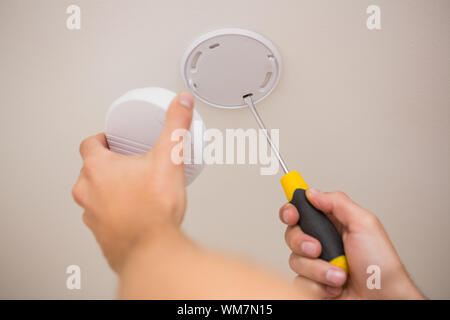 Handyman installing smoke detector with screwdriver on the ceiling Stock Photo