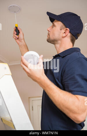 Handyman installing smoke detector with screwdriver on the ceiling Stock Photo