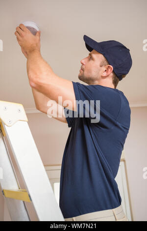 Focused handyman installing smoke detector with screwdriver on the ceiling Stock Photo