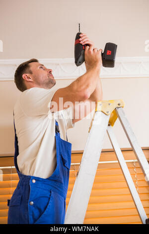 Handyman using a cordless drill to the ceiling in a new house Stock Photo