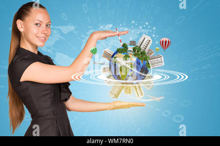 Beautiful businesswoman smiling and looking at camera. Beside is miniature Earth with trees, industrial and residential buildings, air balloons, airpl Stock Photo