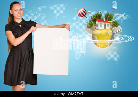 Beautiful businesswoman holding blank paper sheet. Beside is miniature Earth with trees, small house, high-rise buildings, air balloons, airplane, and Stock Photo