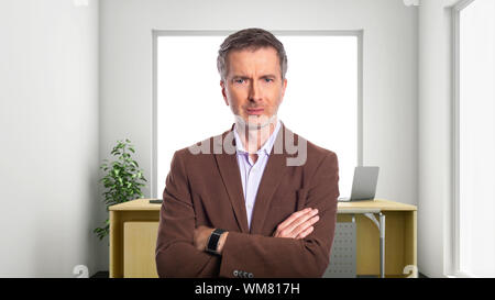 Middle-Aged businessman with gray hair and wearing a brown jacket standing in an office.  Depicts startup and corporate business.  He is looking upset Stock Photo