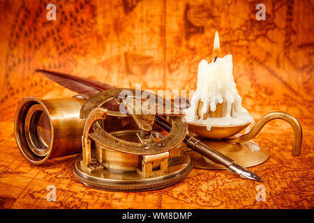 Vintage compass, magnifying glass, quill pen, spyglass lie on an old ancient map in 1565 with a lit candle. Vintage still life. Stock Photo
