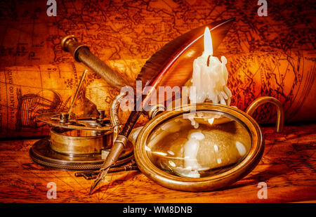 Vintage compass, magnifying glass, pocket watch, quill pen, spyglass lie on an old ancient map in 1565 with a lit candle. Vintage still life. Stock Photo