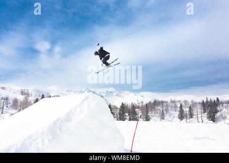 Free style skier performing a high jump. Ski lifts in the mountains in the background. Stock Photo