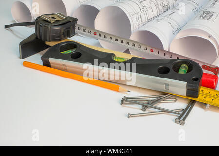 Drawing rolls, hammer, nails, builder's level, pencil, ruler and tape measure on white surface Stock Photo