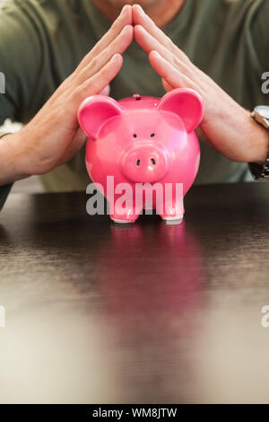 Mid section of a man with joined hands on piggy bank at home in the living room Stock Photo