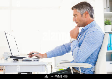 Man in shirt using laptop and thinking in his office Stock Photo