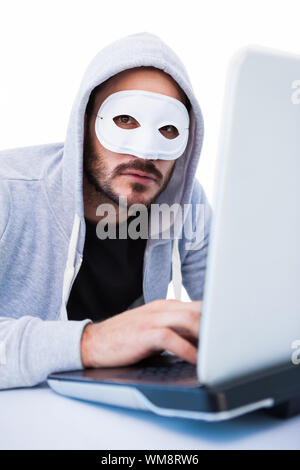 Man wearing mask while hacking into laptop on white background Stock Photo