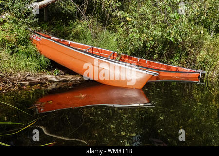 Two orange canoes at a lakeshore of X Lake reflecting the late afternoon sun, Talkeetna, Alaska Stock Photo