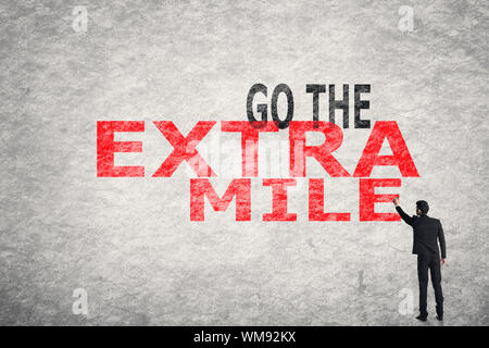 Asian businessman write text on wall, Go To Extra Mile Stock Photo