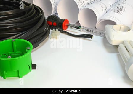 Drawing rolls, triple cable, screwdrivers, test pen, terminal block, wall socket, socket box, lamp on white surface Stock Photo