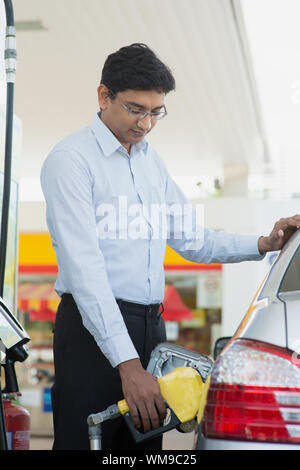 Pumping gas. Asian Indian man pumping gasoline fuel in car at gas station. Stock Photo