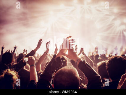 Vintage style photo of a crowd, happy people enjoying rock concert, raised up hands and clapping of pleasure, active night life concept Stock Photo