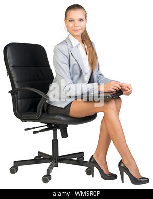 Businesswoman on office chair, holding closed laptop on her knees, looking at camera. Isolated over white background Stock Photo