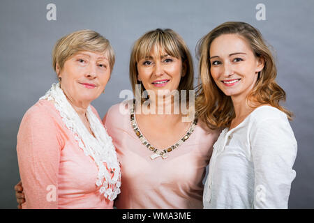 Three generations of attractive women with blond hair and a striking family resemblance posing together arm in arm looking at the camera with friendly Stock Photo