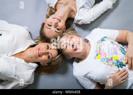 Three generations of attractive women with blond hair and a striking family resemblance posing together arm in arm looking at the camera with friendly Stock Photo