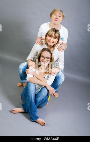 Three generations of attractive women with blond hair and a striking family resemblance posing together arm in arm looking at the camera with friendly Stock Photo