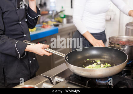 Chef or cook braising meat in a non-stick frying pan over a gas hob as she prepares a meal in a commercial restaurant kitchen