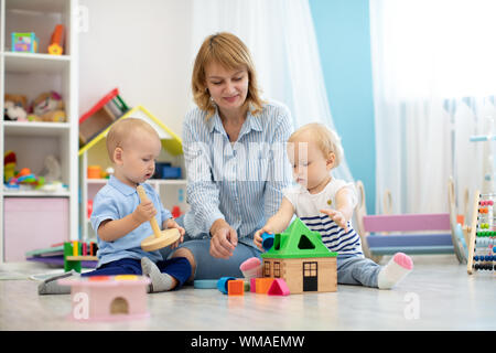 Children with teacher playing with educational toys in kindergarten. Babies with carer in creche or nursery school Stock Photo