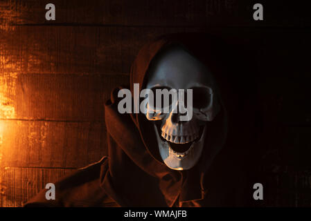 Halloween costume ghost scary skeleton wearing a hooded coat / Grim reaper with skull in black hood on the dark Stock Photo