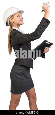 Businesswoman wearing hard hat, holding clipboard, drawing or writing something up in the air. Isolated over white background Stock Photo