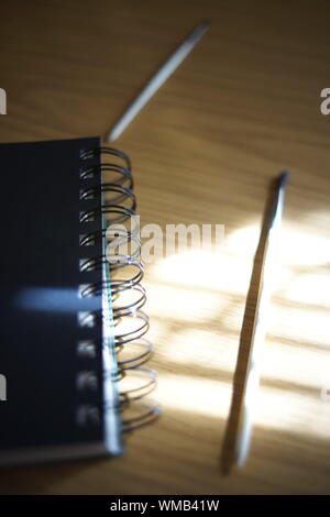 Black notebook on a spiral, brush and pencil on a table with sunshine and shadows. Materials for creativity. Stock Photo